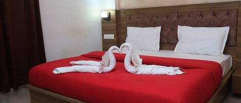 A hotel room with a red bedspread, a wooden headboard, white pillows, and a wall-mounted light.