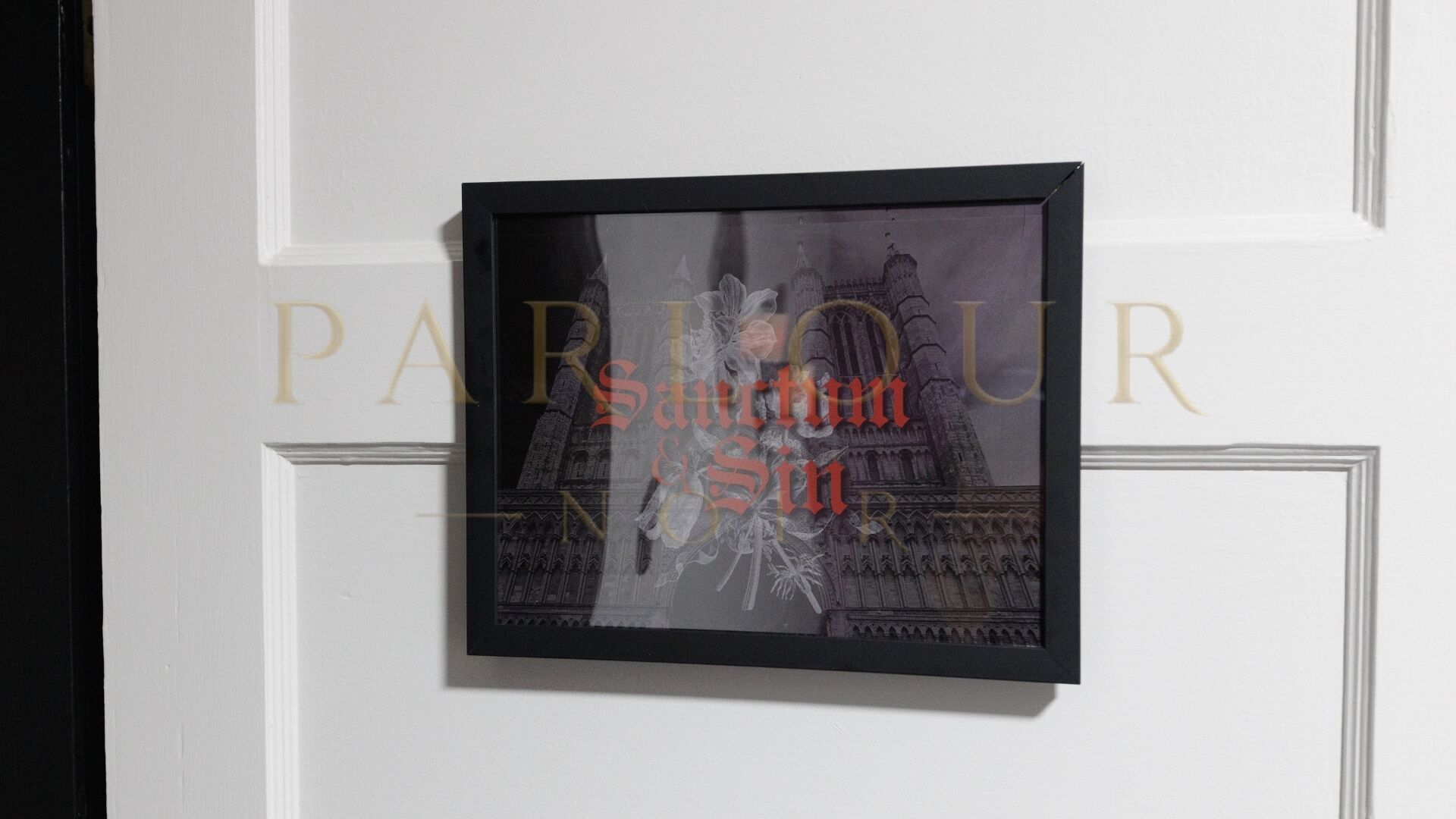 A framed photograph of a historical building with ornate architecture, mounted on a white wall with a decorative panel.