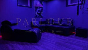 A room with a blue-lit ambiance, featuring a sofa, a chair, and a large poster on the wall.