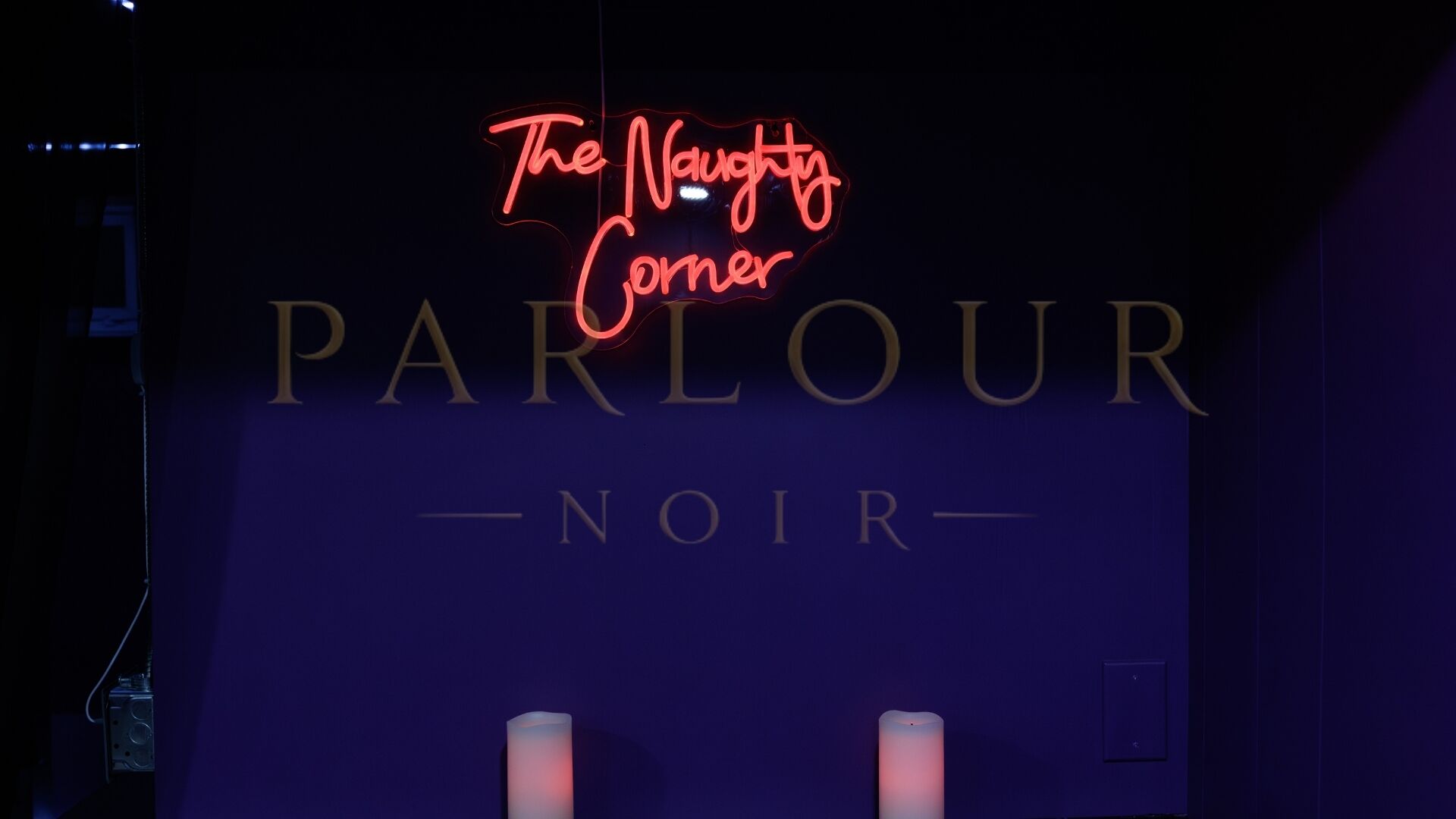 Ein Neonzeichen mit der Aufschrift 'The Naughty Corner' über dem Wort 'PARLOUR' und darunter 'NOIR'.