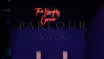 Ein Neonzeichen mit der Aufschrift 'The Naughty Corner' über dem Wort 'PARLOUR' und darunter 'NOIR'.