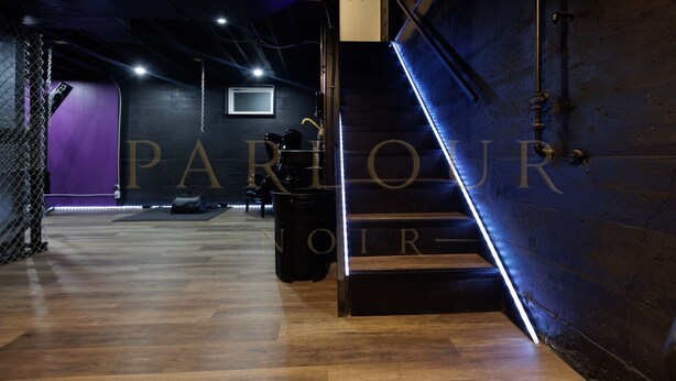 A modern interior with a wooden floor, a staircase with a neon light, and a wall with the word "PARLOUR" partially visible.