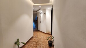 A hallway with white walls, a marble floor, and a potted plant. - Hotel Silky Palace (New Delhi)