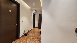 A hallway with dark wooden doors, a marble floor, and a potted plant. - Hotel Silky Palace (New Delhi)