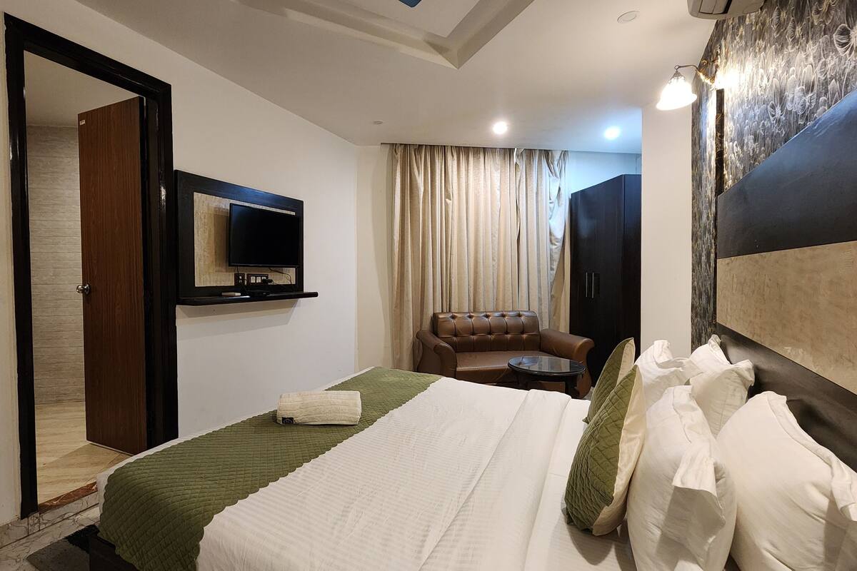 A hotel room with a bed, a television, a brown leather armchair, a small round table, and a wardrobe.
