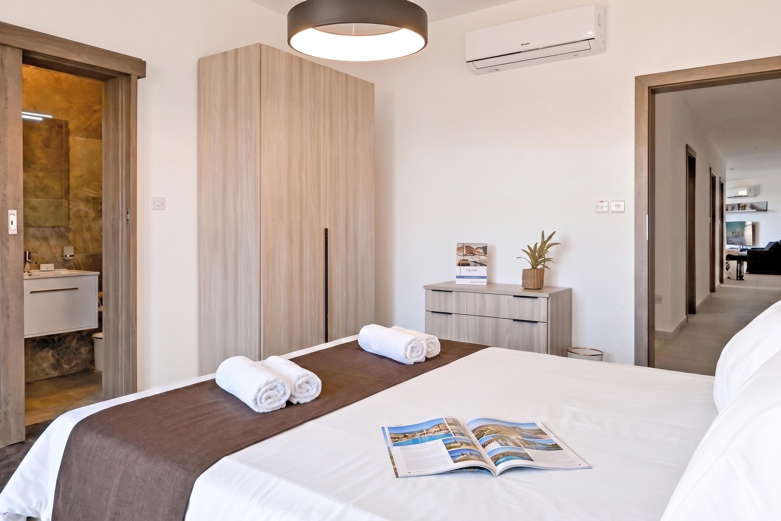 A hotel room with a bed, a bedside table with a magazine, a mirror, and a wardrobe.