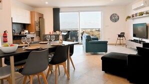 Eine moderne Küche mit Essbereich, ein Wohnzimmer mit Fernseher und ein Balkon mit Blick auf die Stadt.