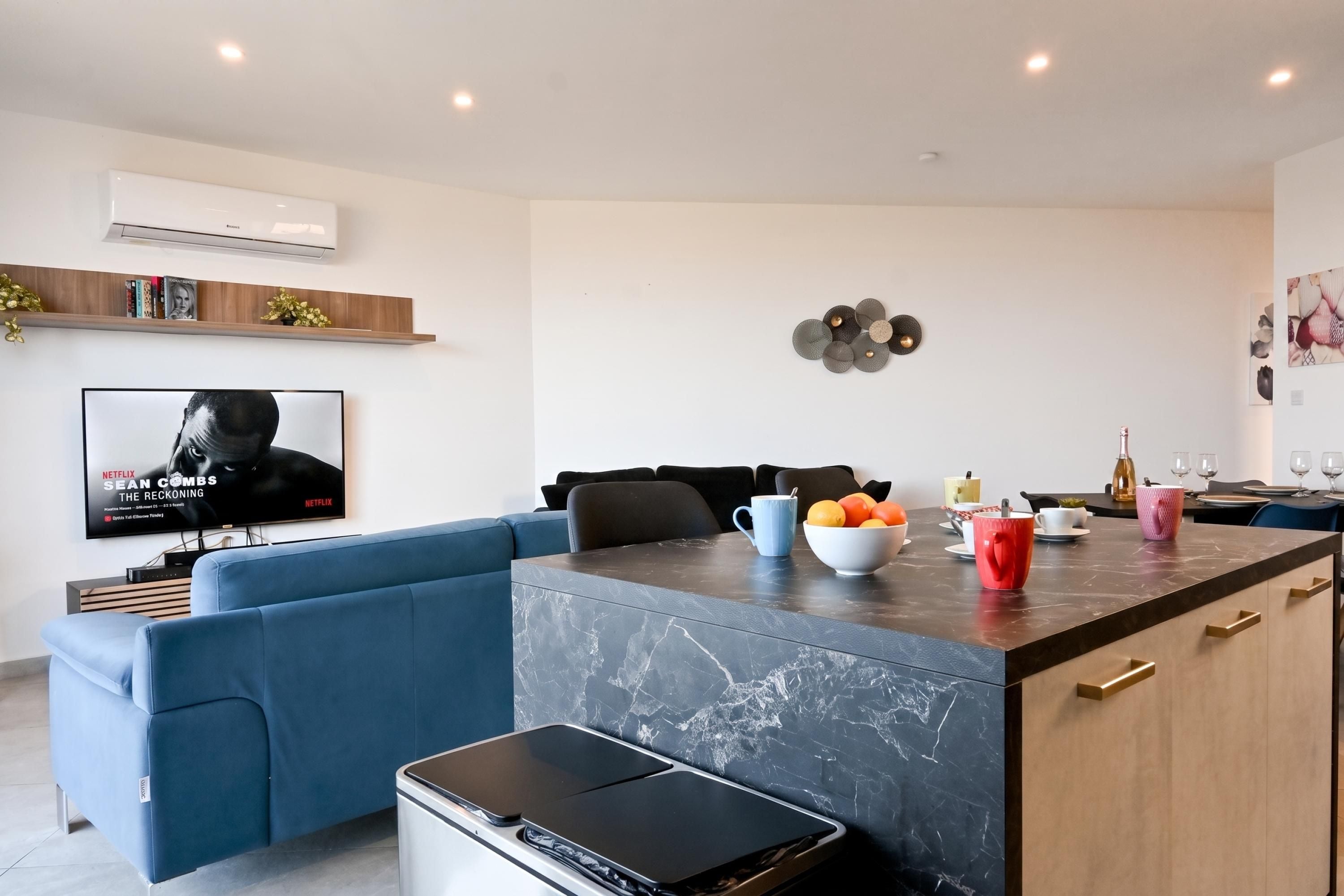 A modern living room with a blue sofa, a coffee table with fruits, and a TV displaying a movie poster.