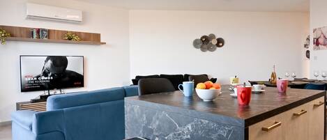 A modern living room with a blue sofa, a coffee table with fruits, and a TV displaying a movie poster.