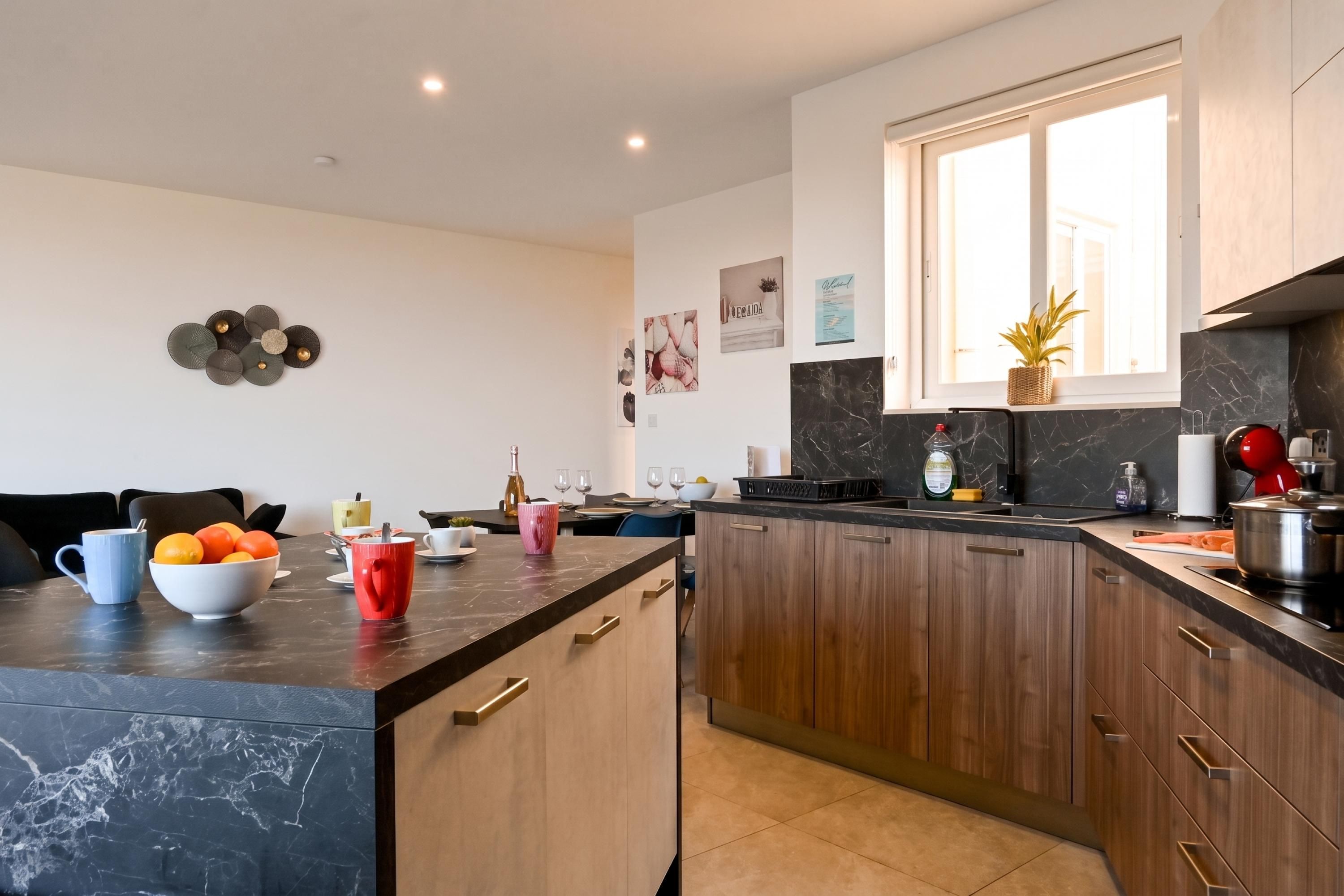 Une cuisine moderne avec des plans de travail sombres, des meubles en bois et une grande fenêtre.