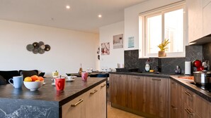 A modern kitchen with dark countertops, wooden cabinets, and a large window. - Sunny Bay View + shared pool Gozo (Xaghra)