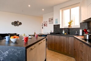 A modern kitchen with dark countertops, wooden cabinets, and a large window. - Sunny Bay View + shared pool Gozo (Xaghra)