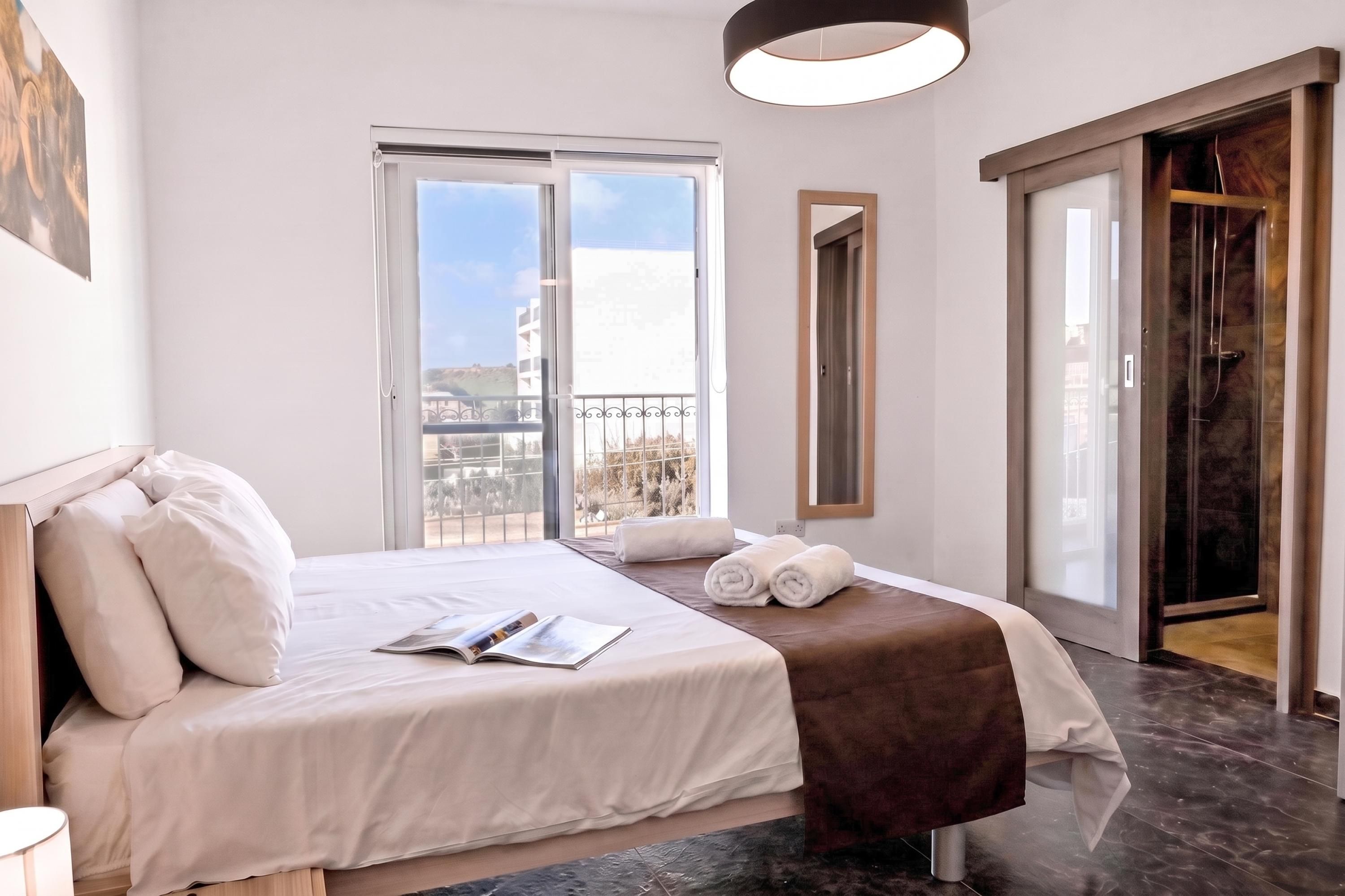 A hotel room with a bed, a window, a door, and a view of the outside.