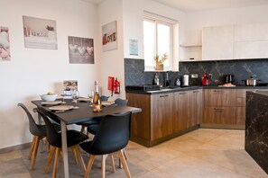 A modern kitchen with a central island, wooden cabinets, and a dining area with chairs and a table set for four. - Sunny Bay View + shared pool Gozo (Xaghra)