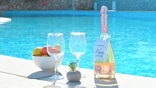 A poolside setting with a bottle of rosé wine, two glasses, and a bowl of fruit. - Sunny Bay View + shared pool Gozo (Xaghra)