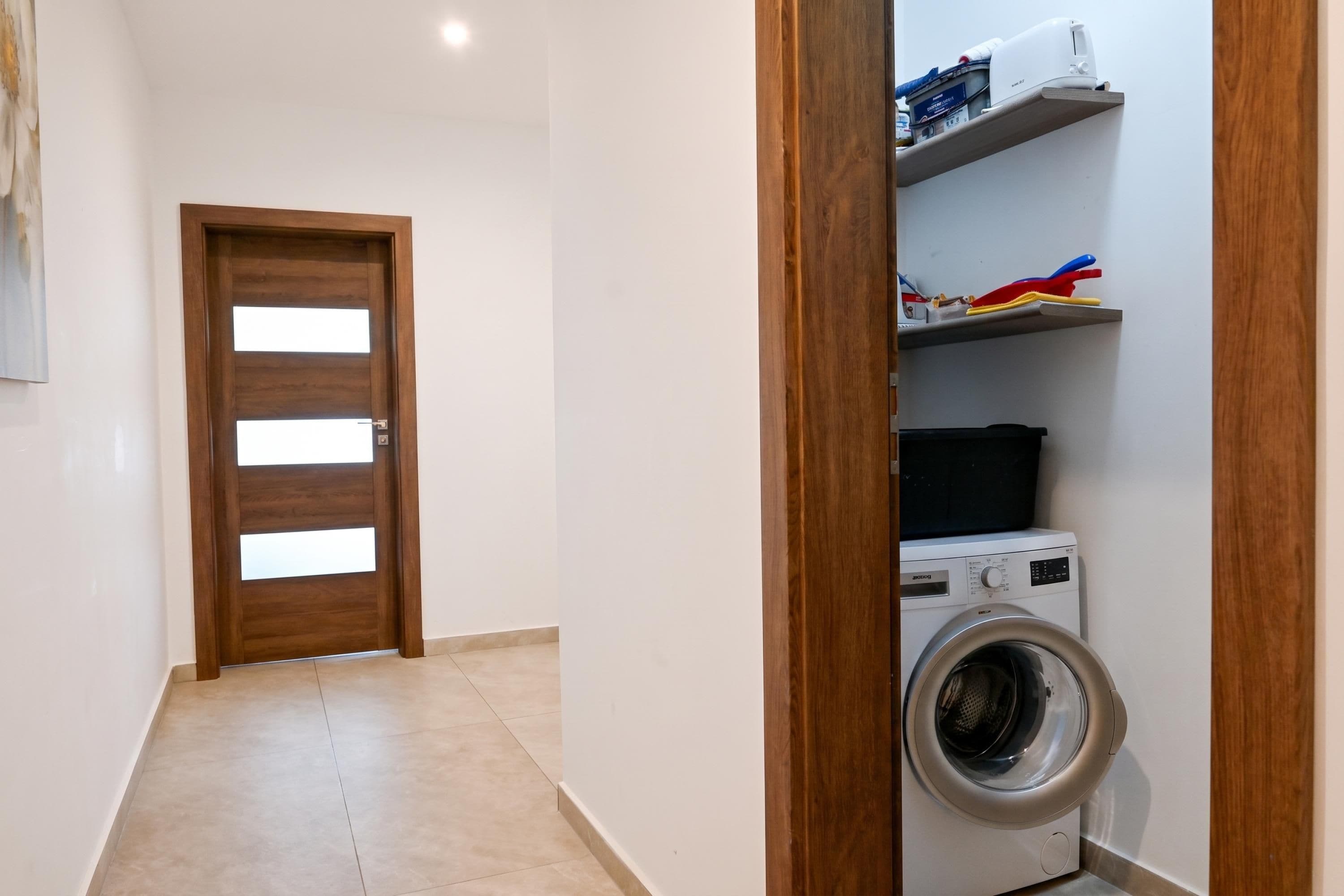 Une buanderie équipée d’un lave-linge, d’étagères contenant des produits de nettoyage et d’une porte en bois.