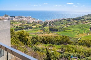 A coastal cityscape with buildings, green fields, and a view of the sea. - Sunny Bay View + shared pool Gozo (Xaghra)
