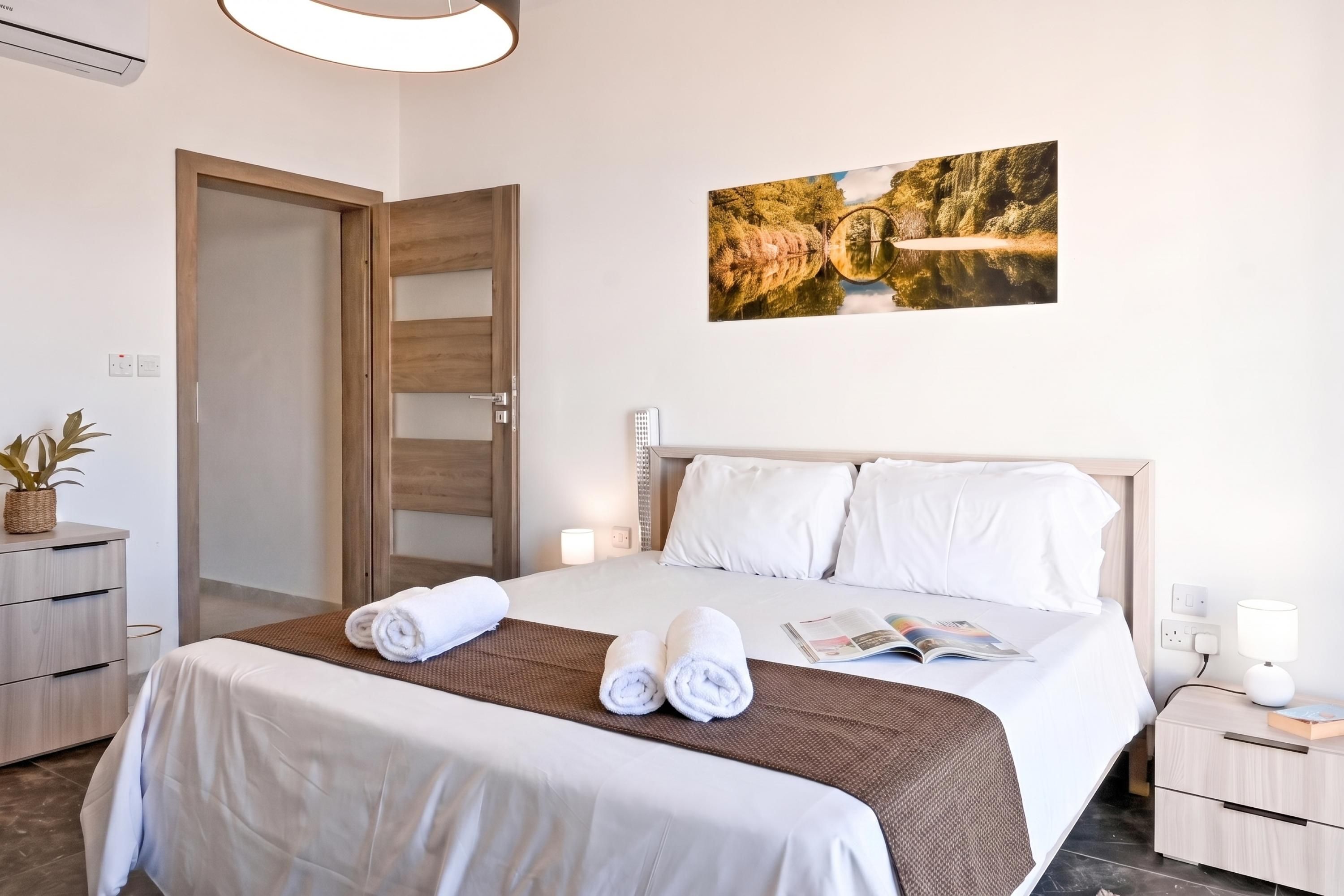 Una camera d'albergo con un letto, comodini, un quadro appeso al muro e una porta.