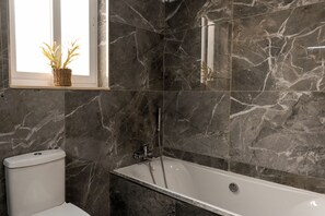 A bathroom with a bathtub, a toilet, and a window with a plant.