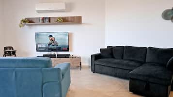 A living room with a flat-screen TV, a black sofa, a blue sofa, and a wooden coffee table.
