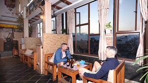 A cozy room with wooden furniture, a tiled floor, and large windows offering a city view. - Hotel De Universal (Kathmandu)