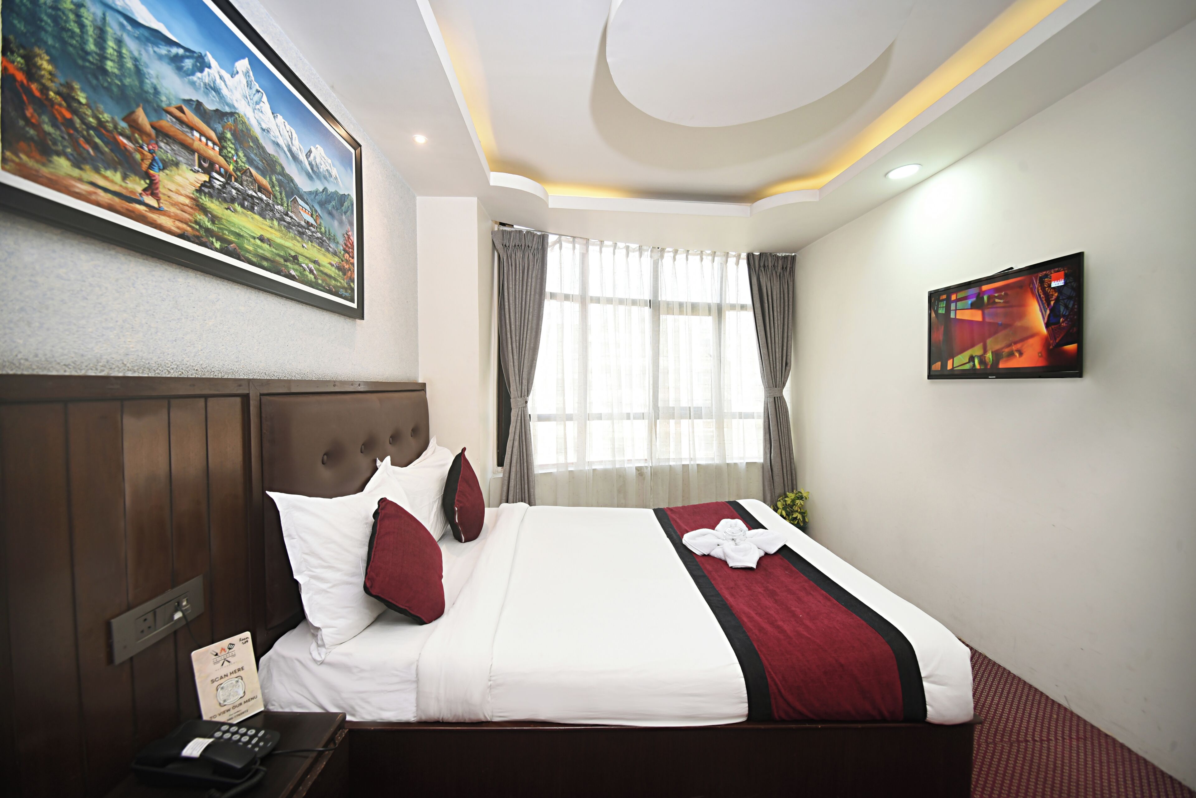 A hotel room with a large bed, a television, a painting on the wall, and a window with curtains.