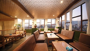 A restaurant with wooden furniture, large windows, and a city view. - Hotel De Universal (Kathmandu)