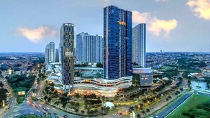 A modern high-rise building with a curved facade, surrounded by a busy urban area with visible roads and greenery. - Gatotkaca Hotels (Surabaya)
