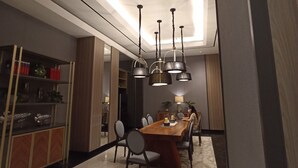 A modern dining area with a long wooden table, multiple chairs, and pendant lights. - Gatotkaca Hotels (Surabaya)