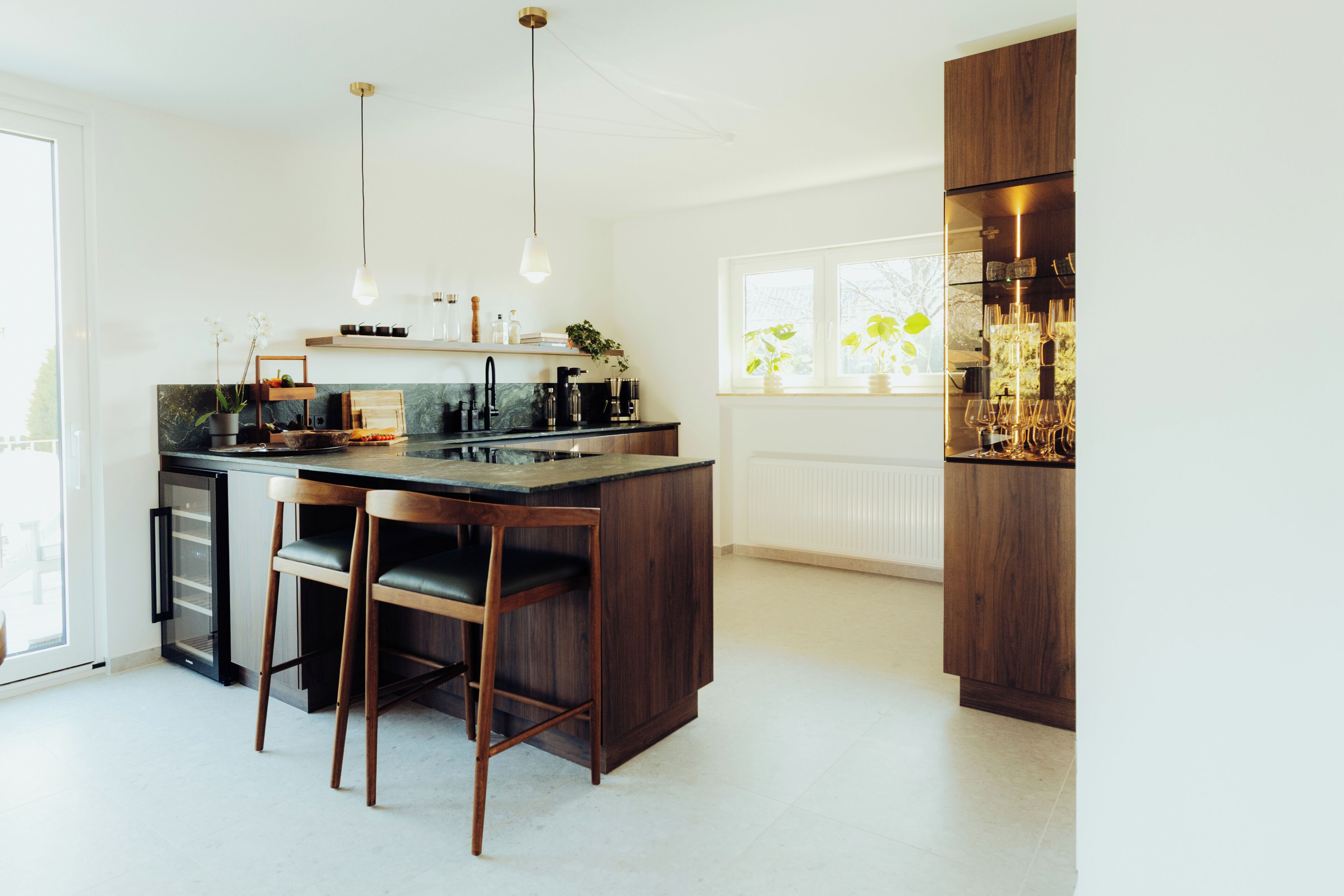 A modern kitchen with a central island, bar stools, pendant lighting, and a view of the outdoors through a window.