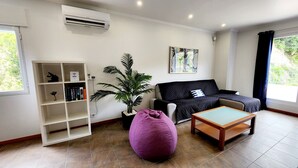 A modern living room with a black sofa, a wooden coffee table, a purple bean bag, a bookshelf, and a potted plant.
