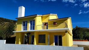 A two-story yellow building with a balcony, large windows, and a chimney.