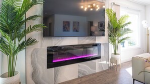 Ein modernes Wohnzimmer mit einem großen Flachbildfernseher, der an einer Marmorwand angebracht ist, einem integrierten Aquarium darunter und zwei großen Kübelpflanzen.
