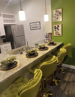 A modern kitchen with a granite countertop, stainless steel appliances, and green walls. There are bar stools and a 'KITCHEN' sign on the wall. - Charming Cozy 2-bedroom apartment in Jacksonville Florida (Jacksonville)