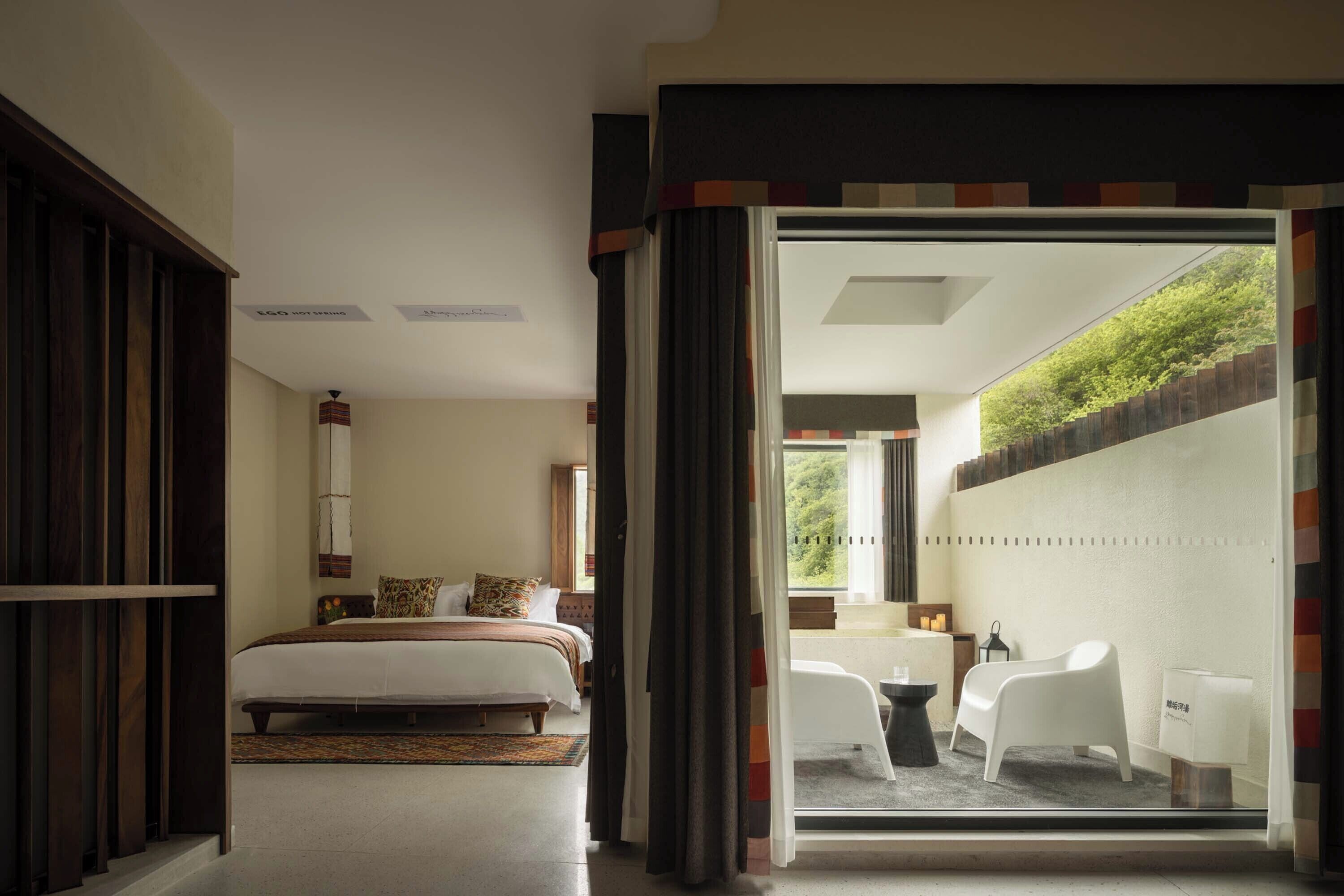 A hotel room with a bed, a desk, and a view of a garden through a sliding door.