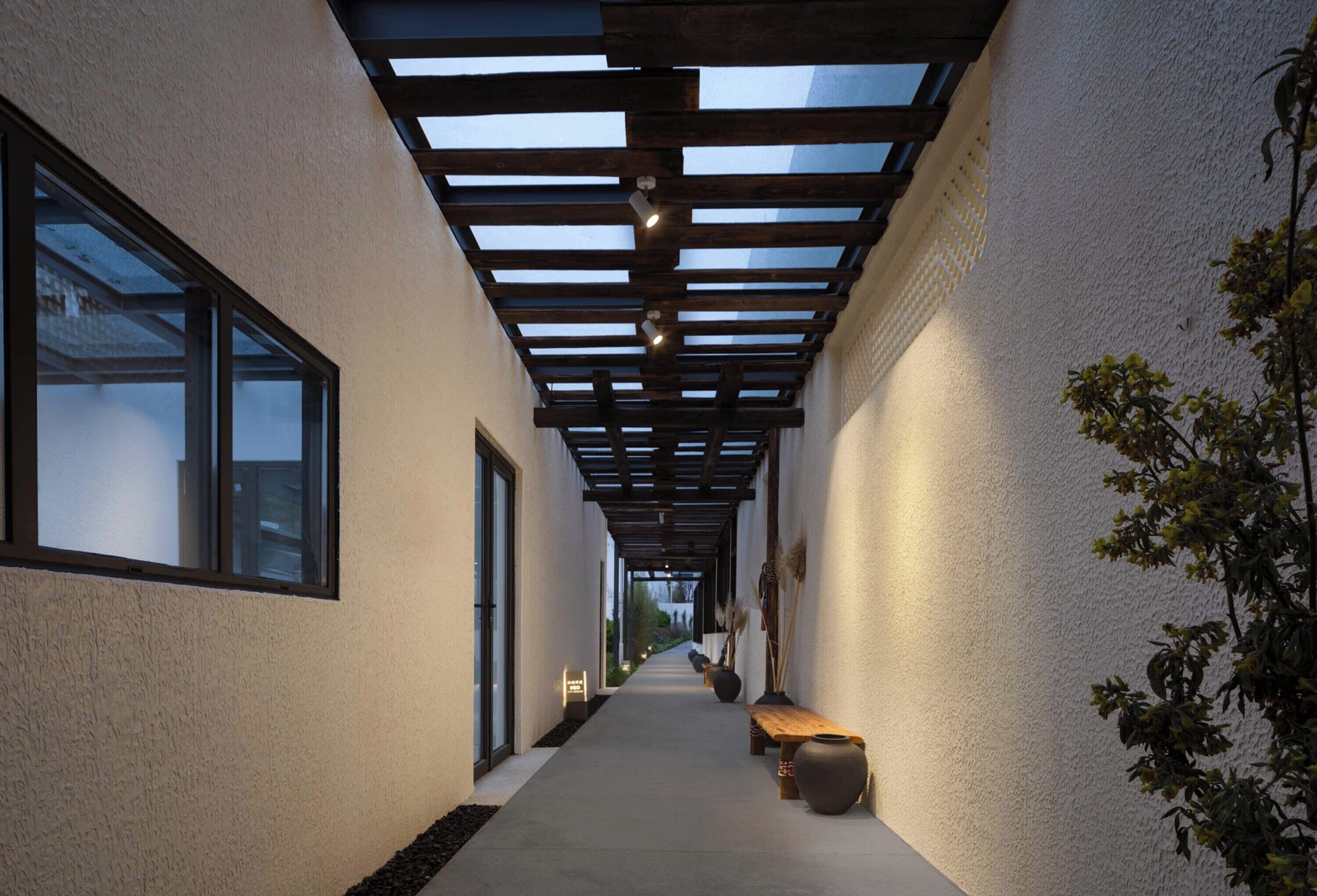 A corridor with a wooden ceiling, a bench, and a potted plant.