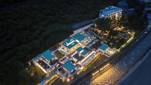 An aerial view of a modern hotel with multiple swimming pools, a large building with illuminated windows, and a well-lit outdoor area. - EGO Hot Spring Resort Hotel (Garze)