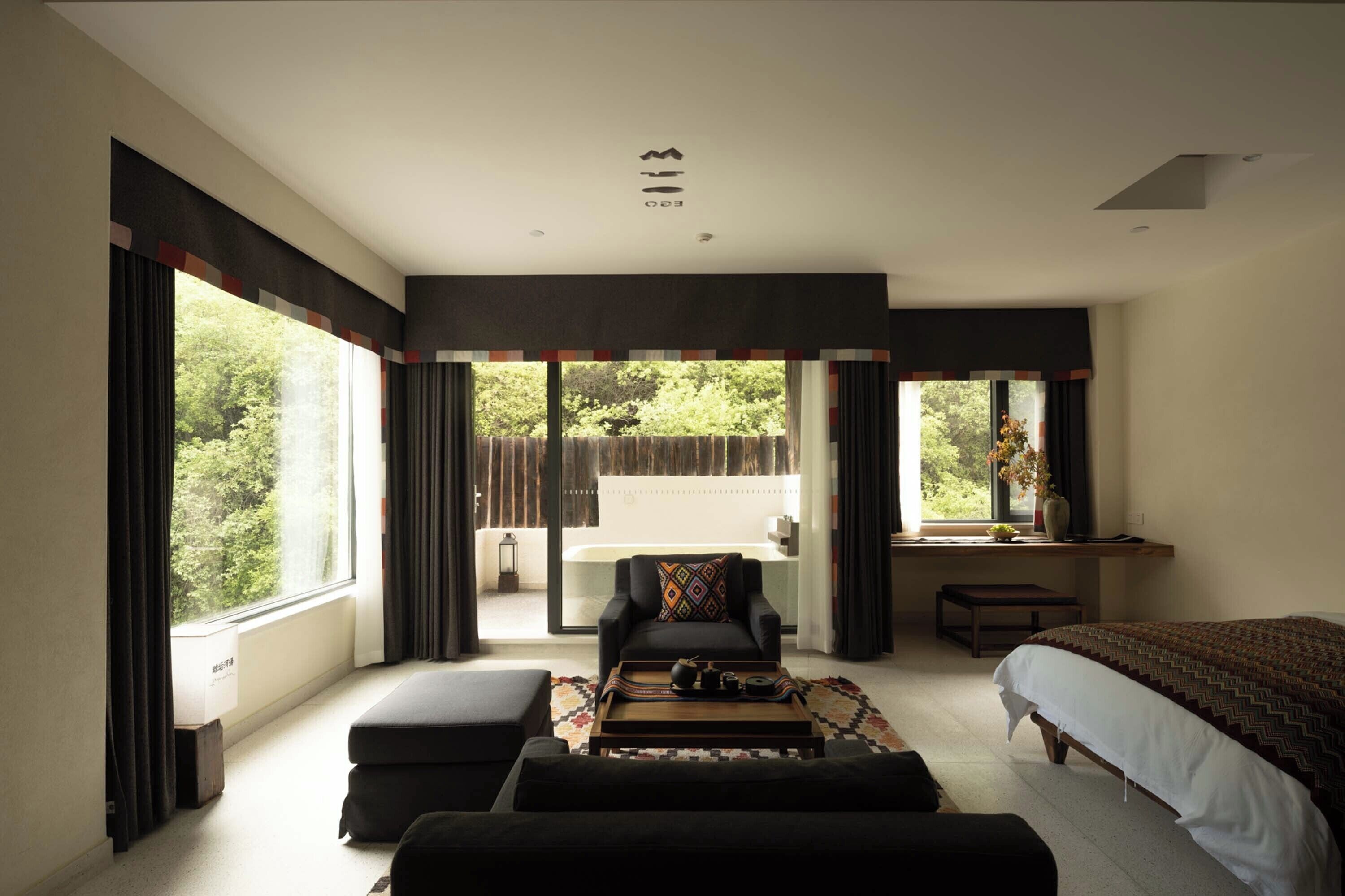 A modern bedroom with a large bed, a sofa, a coffee table, and a view of the outdoors.