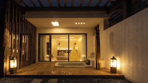 A modern house with a wooden deck, a sliding glass door entrance, a small outdoor seating area, and a lantern on the right. - EGO Hot Spring Resort Hotel (Garze)