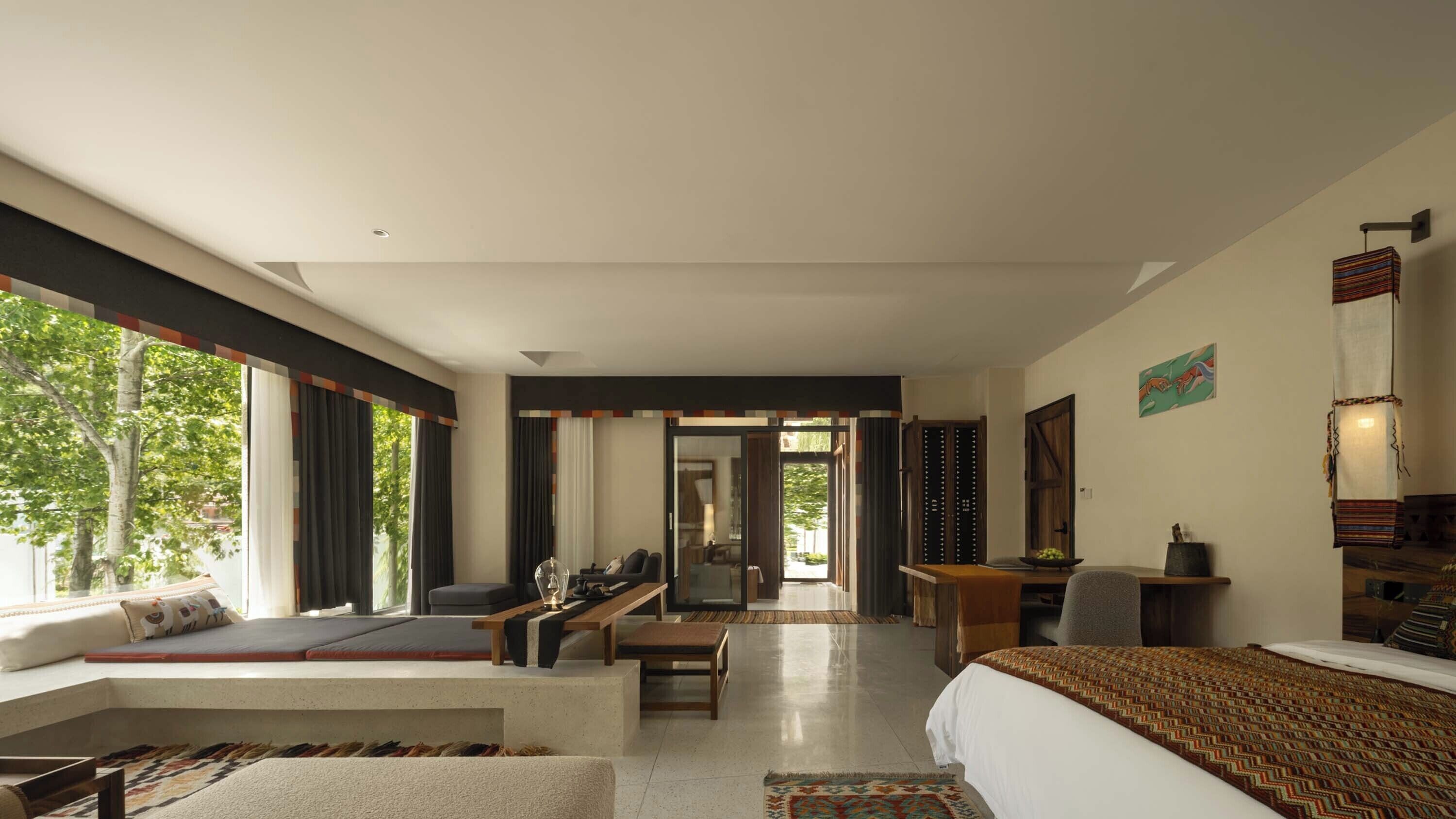 A modern hotel room with a large bed, a sofa, a dining area, and a view of the outdoors.