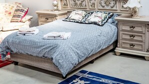 Een slaapkamer met een groot bed, een versierd hoofdeinde, nachtkastjes en een decoratief vloerkleed.