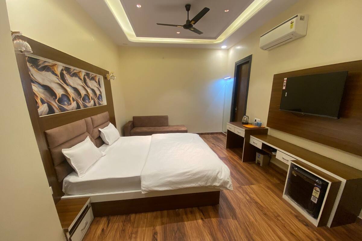 A hotel room with a large bed, a flat-screen TV, a ceiling fan, and an air conditioning unit.