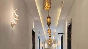 A long, narrow hotel corridor with a shiny floor, blue stripe on the walls, and a series of hanging lights. - Pink Mahal Hotel And Resort (Amer)