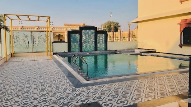 A swimming pool with a geometric tile pattern, a glass enclosure with decorative panels, and a traditional building with arched windows. - Pink Mahal Hotel And Resort (Amer)