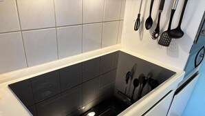 Een keuken met een zwart inductiefornuis, een inbouwoven en een messenhouder met diverse keukengerei.