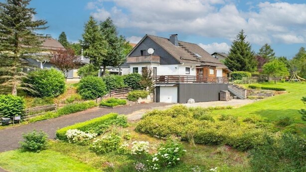 Een twee verdiepingen tellend huis met een schuin dak, een omheinde tuin en een verzorgde tuin.