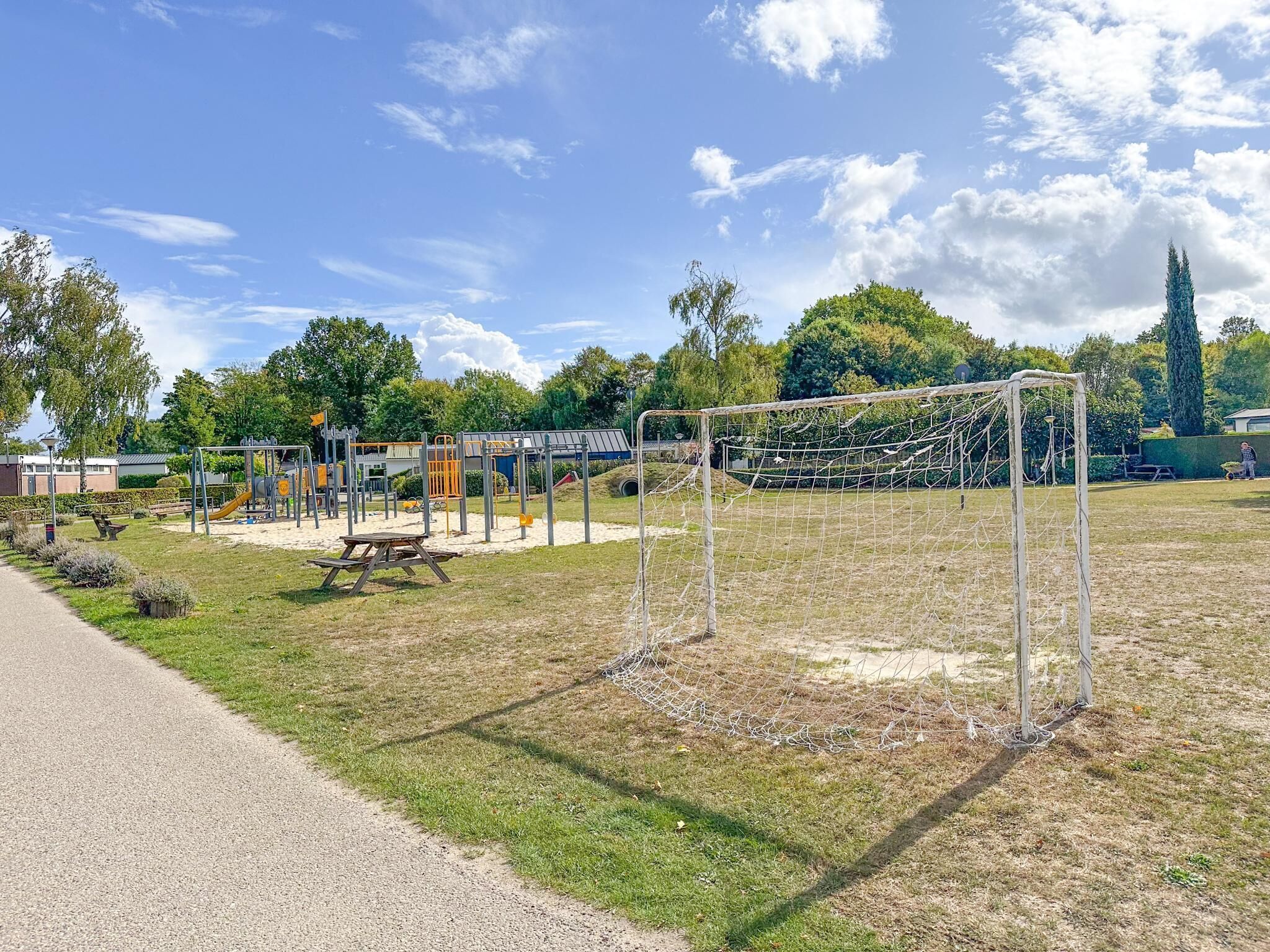 A playground with various play structures, a soccer goal, and a paved path.