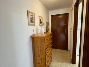 Ein Flur mit einem hölzernen Kommodenstück, einer Tür und zwei gerahmten Bildern an der Wand.