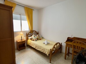 Ein kleines Schlafzimmer mit einem Einzelbett, einem Nachttisch mit Lampe, einem Holztisch und einem Stuhl.