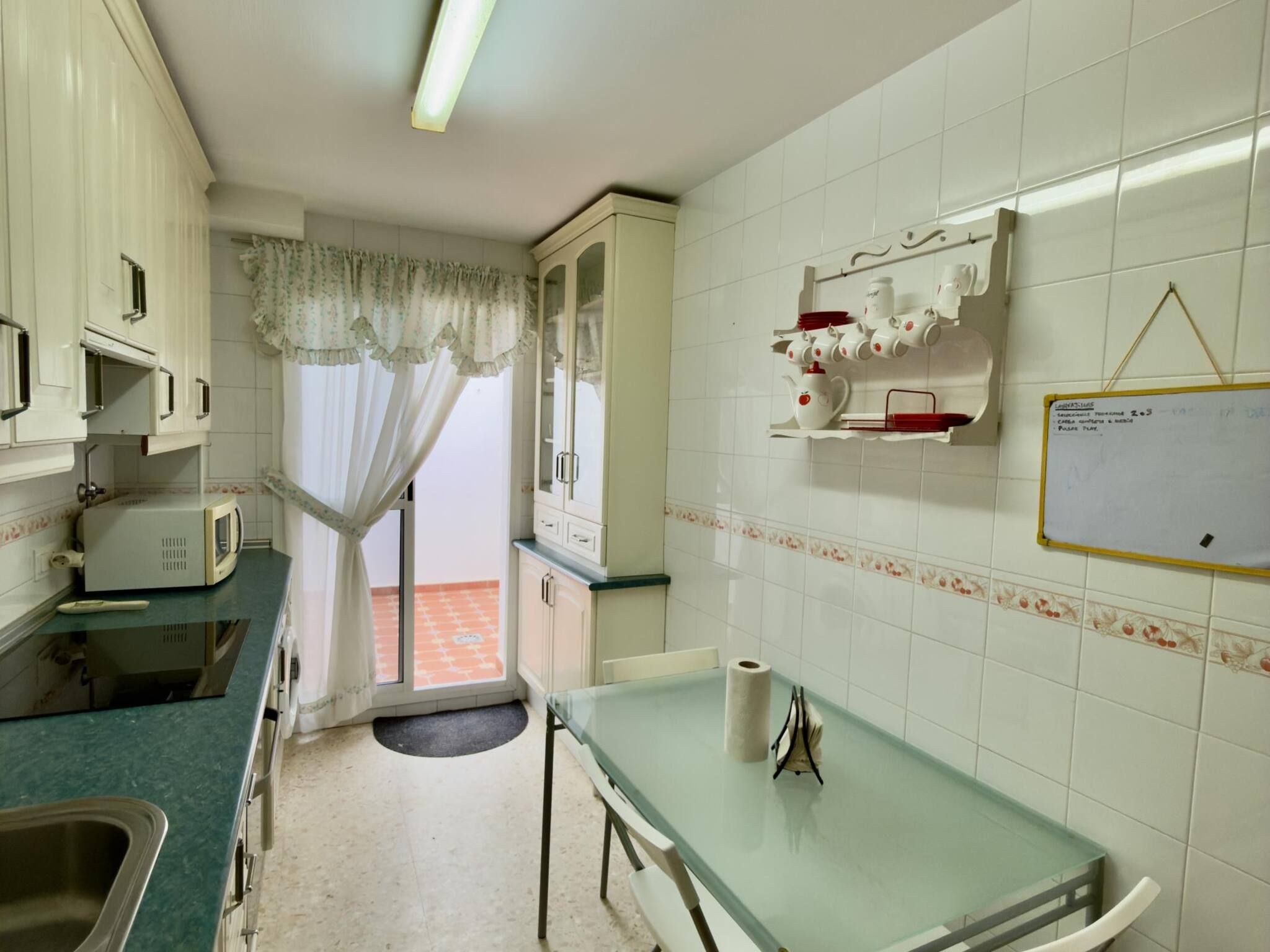 A kitchen with white cabinets, a microwave, a table with a roll of paper towels, and a window with a curtain.